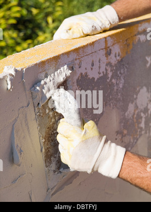Man spreading tile adhesive on a wall in a sunny day. Stock Photo