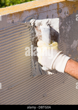 Man spreading tile adhesive with a trowel in a sunny day. Stock Photo