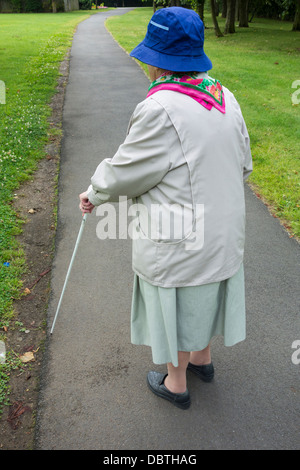 Ninety year old visually impaired lady with white stick walking in public park. England, UK Stock Photo