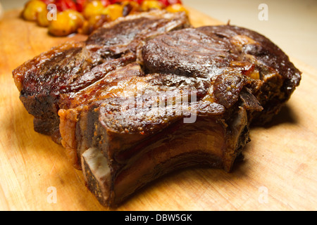 Roast rib of beef on a wooden chopping board, with roasted red and yellow tomatoes Stock Photo