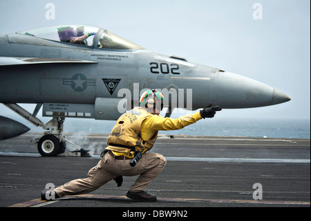 A US Navy Aviation Boatswain Mate signals a F/A-18E Super Hornet fighter aircraft to take off from the flight deck of the aircraft carrier USS Nimitz July 25, 2013 operating in the North Arabian Sea. Stock Photo