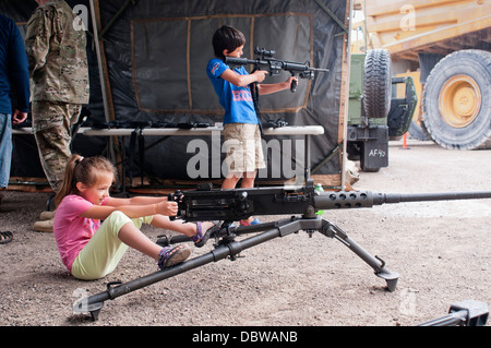 A young girl sits behind a heavy machine gun as a boy plays with an automatic rifle during a static display at the Nautical Festival August 2, 2013 in Rogers City, Michigan. Stock Photo