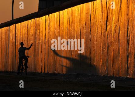 A man drives past the East Side Gallery with his bike in Berlin, Germany, 30 July 2013. Photo: Paul Zinken Stock Photo