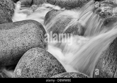 Black and white image of detail of water flowing over round rocks Stock Photo