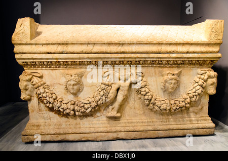 Marble sarcophagus with lid formed as a steeply pitched gable roof, decorated richly in relief with themes relating to beliefs for the afterlife. Along the long side runs a garland with leaves and fruits, held centrally by a small Eros and framing heads of Medusa with snakes and wings on one face and lion heads on the other. The cover of the sarcophagus replicates roof tiles in relief and bears pediments at the edges with eagle and lions among ox head, palmettes and rosettes. It was found under the altar of a Christian basilica and contained bones and golden jewelry. Malia, Roman period, 3rd c Stock Photo