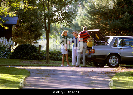 1980s PEOPLE LOADING TRUNK LEAVING ON AUTOMOBILE TRIP SAYING GOODBYE IN SUBURBAN DRIVEWAY Stock Photo