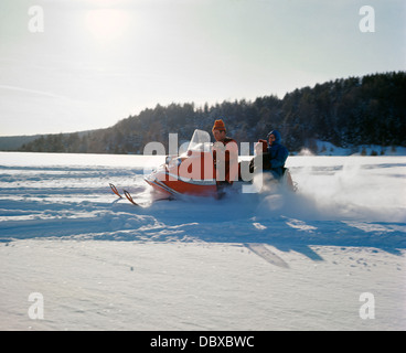 1960 1960s RETRO FAMILY MOTHER FATHER DAUGTHER RIDING ON SNOWMOBILE WINTER SNOW RECREATION Stock Photo