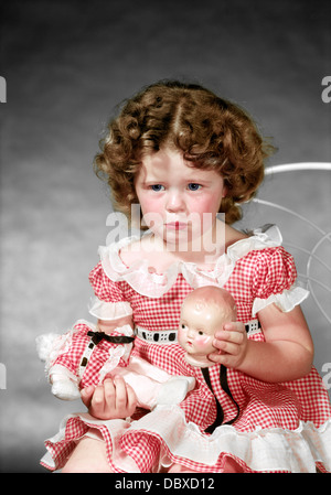 1940s 1950s GIRL WEARING RED GINGHAM CHECKED DRESS CRYING HOLDING BROKEN DOLLS HEAD Stock Photo