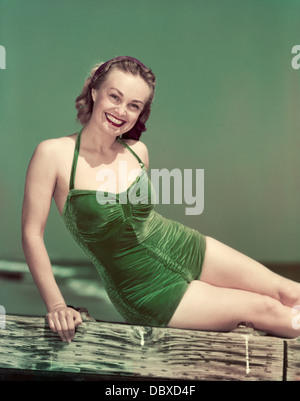 1940s PORTRAIT SMILING WOMAN WEARING GREEN VELVET BATHING SUIT SITTING POSING ON DIVING BOARD Stock Photo