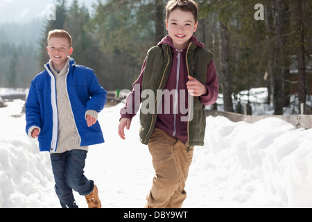 Portrait of happy boys running in snowy lane Stock Photo
