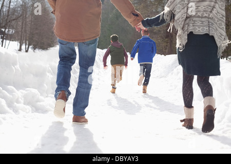 Happy couple holding hands and watching boys run in snowy lane Stock Photo