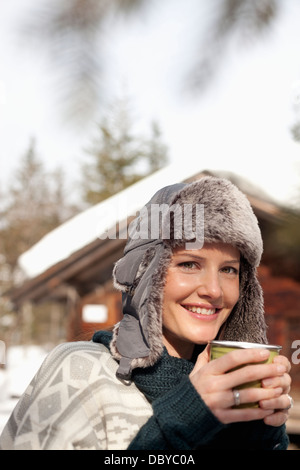 Close up portrait of woman in fur hat drinking coffee outside cabin Stock Photo