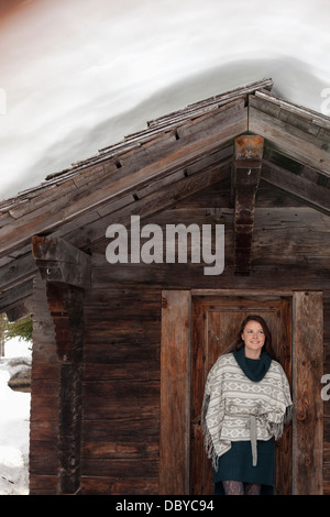 Portrait of smiling woman standing in doorway of snowy cabin Stock Photo