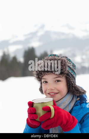 Portrait of smiling boy drinking hot chocolate in snowy field Stock Photo