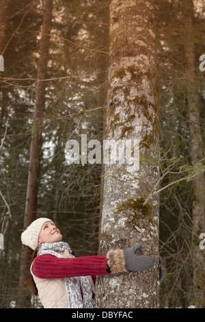Smiling woman hugging tree trunk in woods Stock Photo