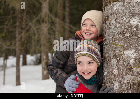 Happy boys leaning against tree trunk in snowy woods Stock Photo