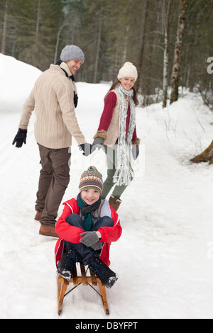 Parents pulling happy boy on sled in snowy woods Stock Photo