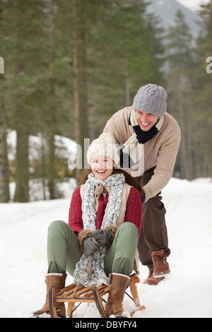 Happy couple sledding in snowy woods Stock Photo