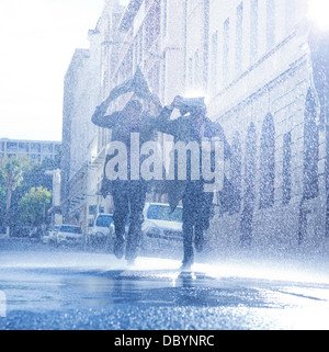 Businessmen covering heads with newspaper in rain Stock Photo