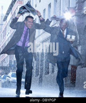 Businessmen carrying coffee and covering heads with newspaper in rain Stock Photo