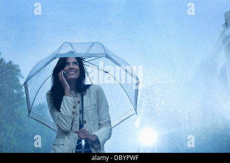 Businesswoman talking on cell phone under umbrella in rain Stock Photo