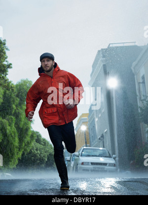 Man in raincoat running in rain Stock Photo