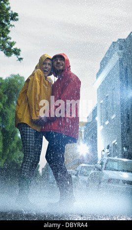Happy couple in raincoats holding hands in rain Stock Photo