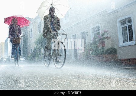 Couple with umbrellas riding bicycles in rain Stock Photo