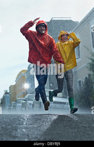Happy couple in raincoats running down street in rain Stock Photo