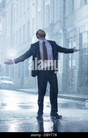 Businessman standing with arms outstretched in rainy street Stock Photo