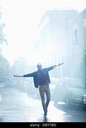 Happy man with arms outstretched in rainy street