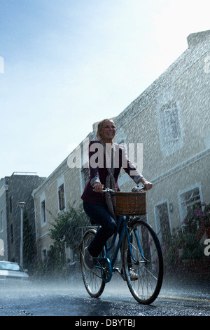 Happy woman riding bicycle in rainy street Stock Photo