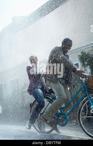 Happy couple riding bicycle in rainy street Stock Photo