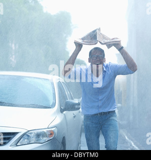 Smiling man holding newspaper overhead in rainy street Stock Photo
