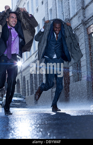 Happy businessmen covering heads with coats in rainy street Stock Photo