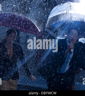 Happy business people running with umbrellas in rain Stock Photo