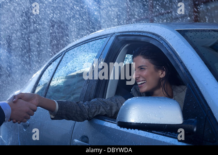 Smiling businesswoman in car extending handshake in rain Stock Photo