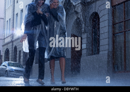 Businesswomen in ponchos walking in rainy street Stock Photo