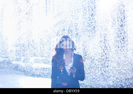 Happy businesswoman text messaging with cell phone in rain Stock Photo