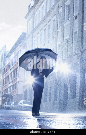 Businesswoman standing under umbrella in rainy street Stock Photo