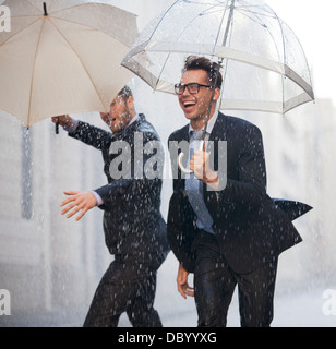 A man walking in the rain holding an umbrella reflected in the wet ...