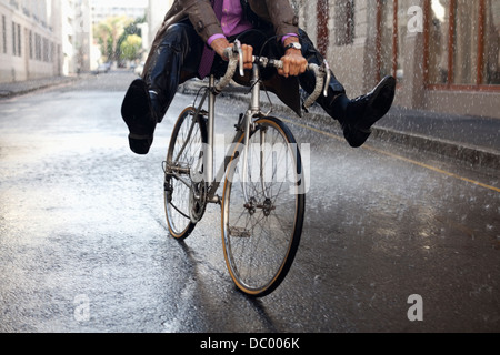 Businessman riding bicycle with feet up in rain Stock Photo