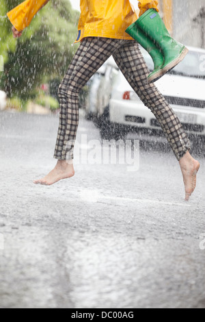 Barefoot woman running across street in rain Stock Photo