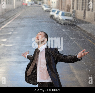 Happy businessman with arms outstretched in rainy street Stock Photo