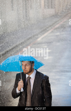 Businessman under tiny umbrella in rainy street Stock Photo
