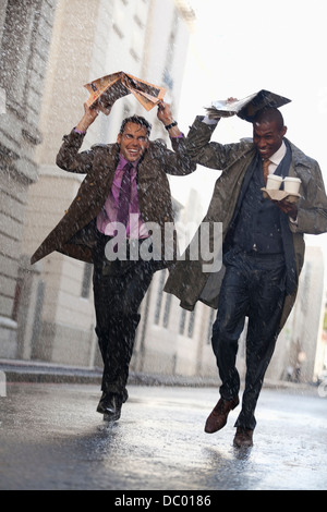 Businessmen with coffee covering heads with newspaper in rainy street Stock Photo