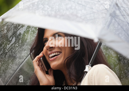 Happy woman talking on cell phone under umbrella in rain Stock Photo