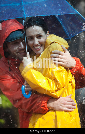 Happy couple hugging under umbrella in rain Stock Photo