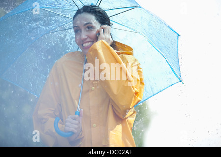 Happy woman talking on cell phone under umbrella in rain Stock Photo