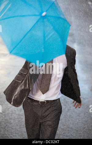 Businessman with tiny umbrella running in rainy street Stock Photo